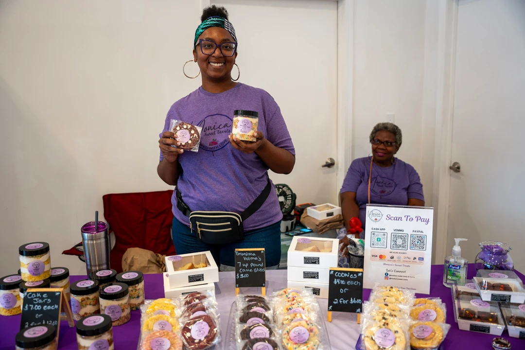 A baker holding dessert jars behind a purple display.