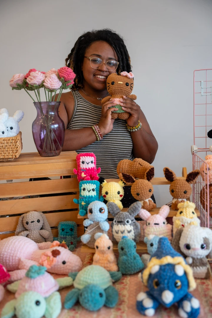 A maker holding a small crocheted animal behind a plush display.