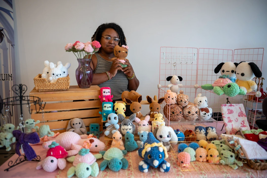 A maker holding a small crocheted animal behind a plush display.