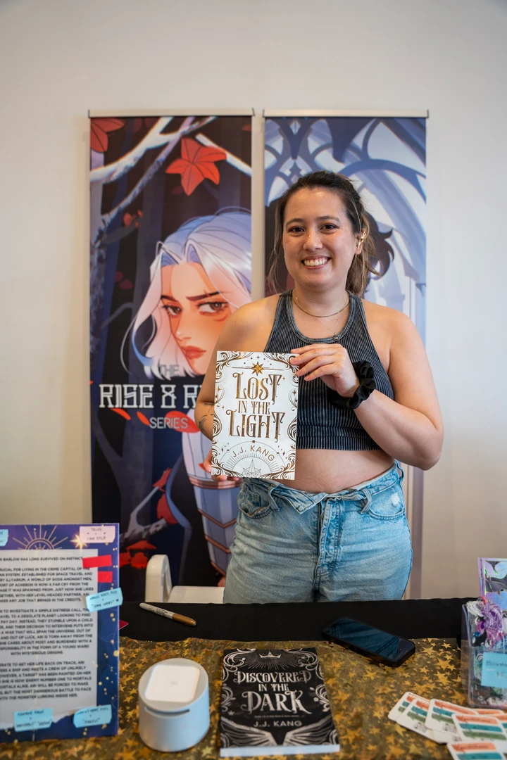 A maker holding a piece beside illustrated posters at a market table.