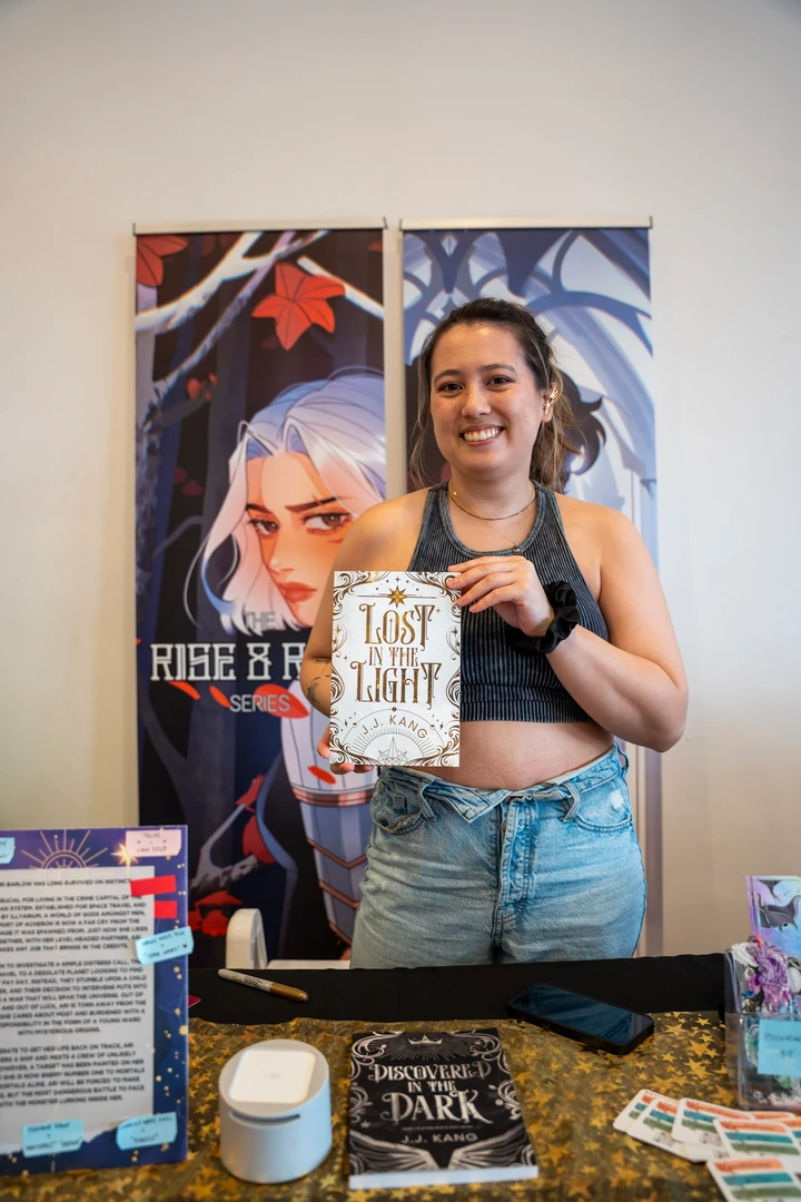A maker holding a piece beside illustrated posters at a market table.
