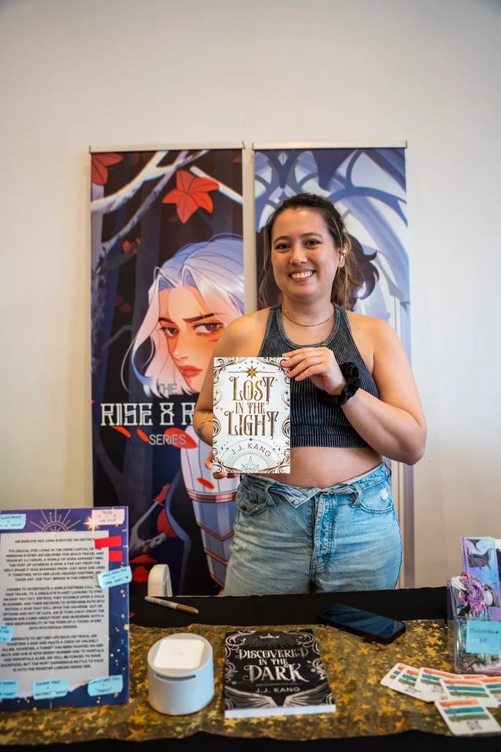 A maker holding a piece beside illustrated posters at a market table.