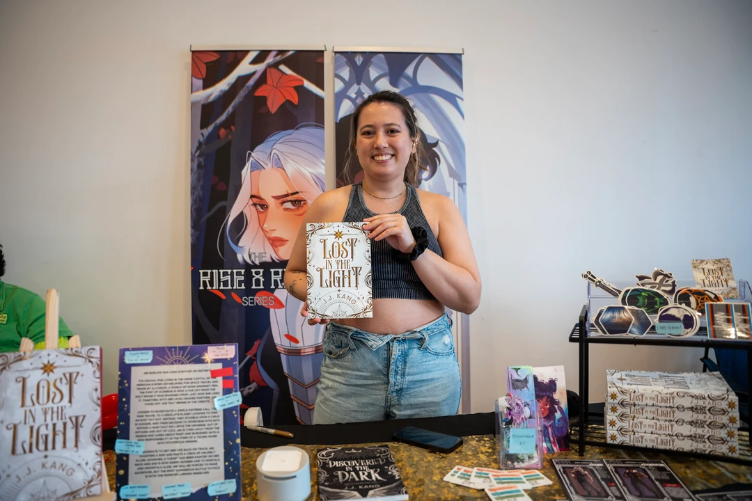 A maker holding a piece beside illustrated posters at a market table.