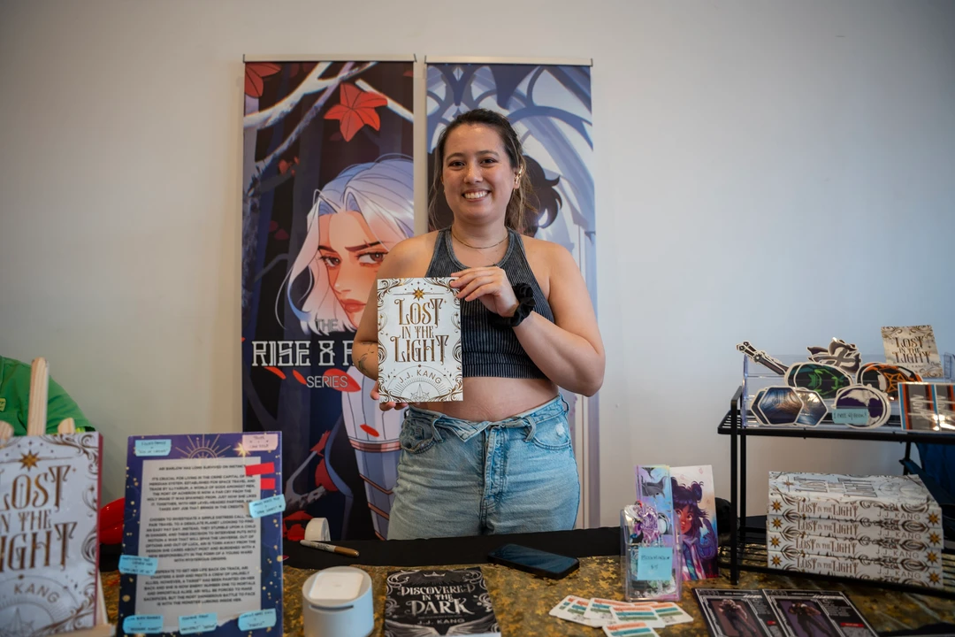 A maker holding a piece beside illustrated posters at a market table.
