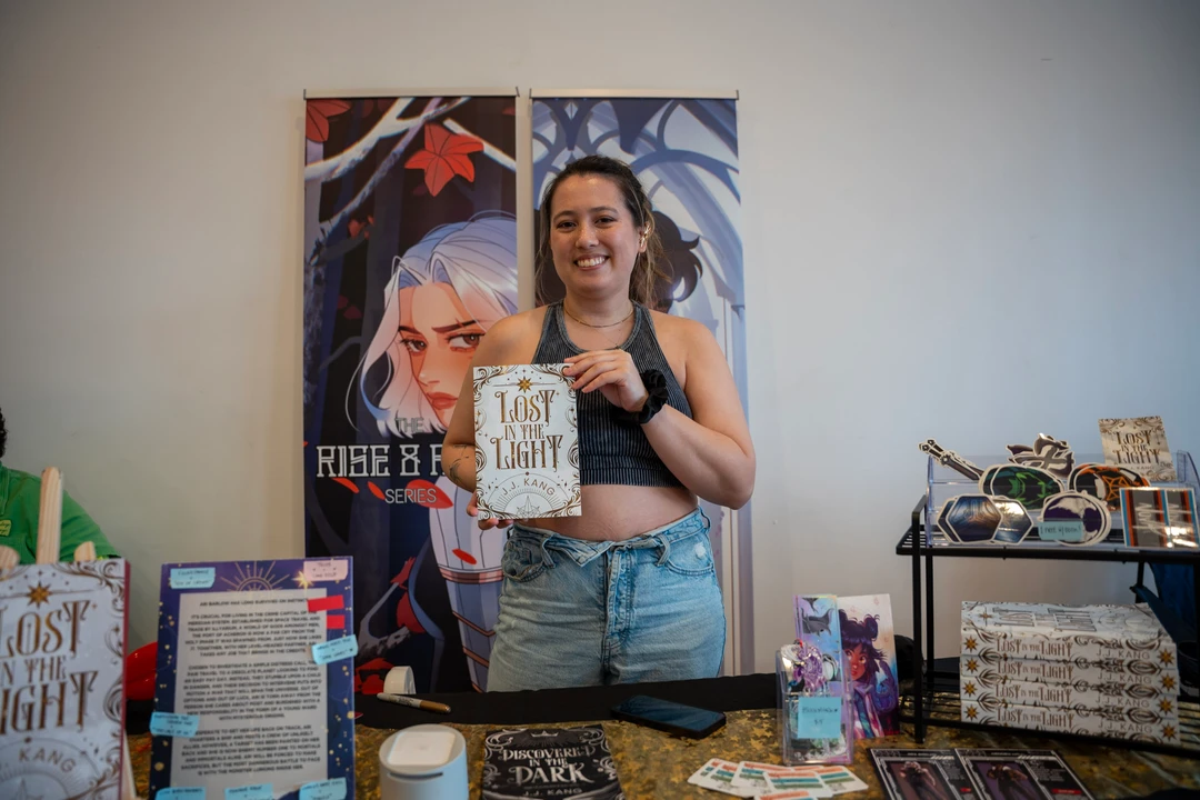 A maker holding a piece beside illustrated posters at a market table.
