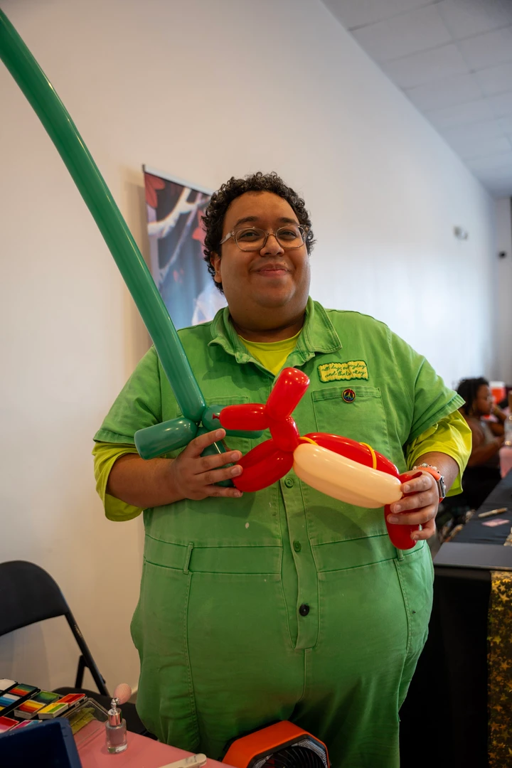 A balloon artist in green holding a balloon creation.