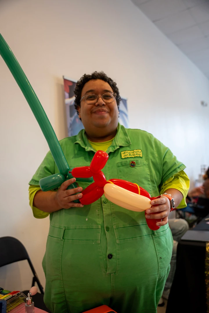 A balloon artist in green holding a balloon creation.