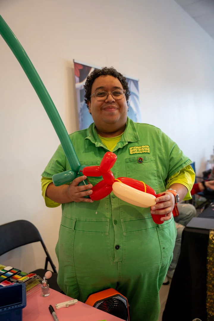 A balloon artist in green holding a balloon creation.