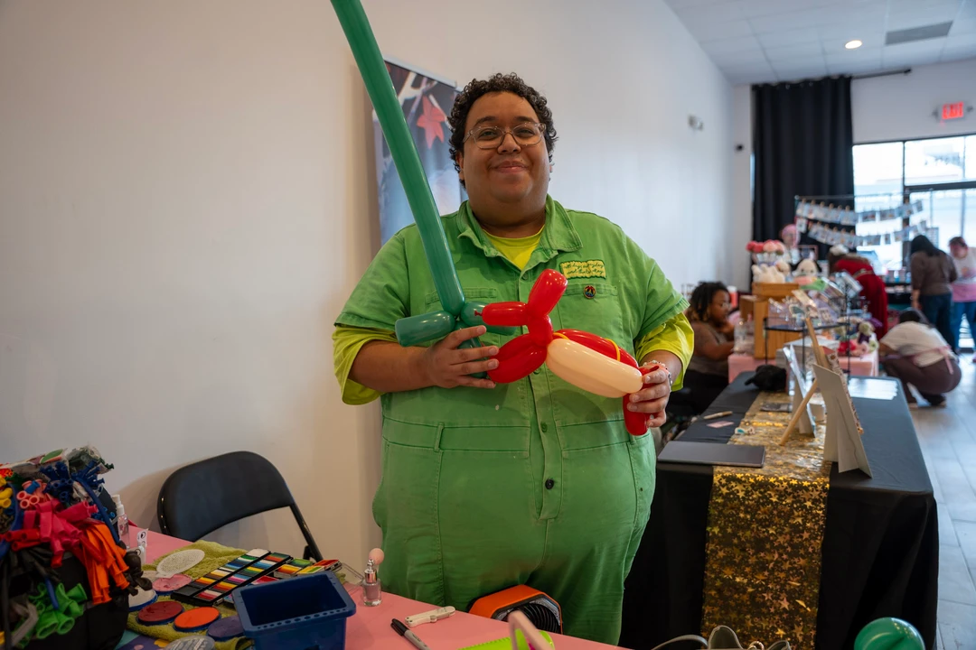 A balloon artist in green holding a balloon creation.