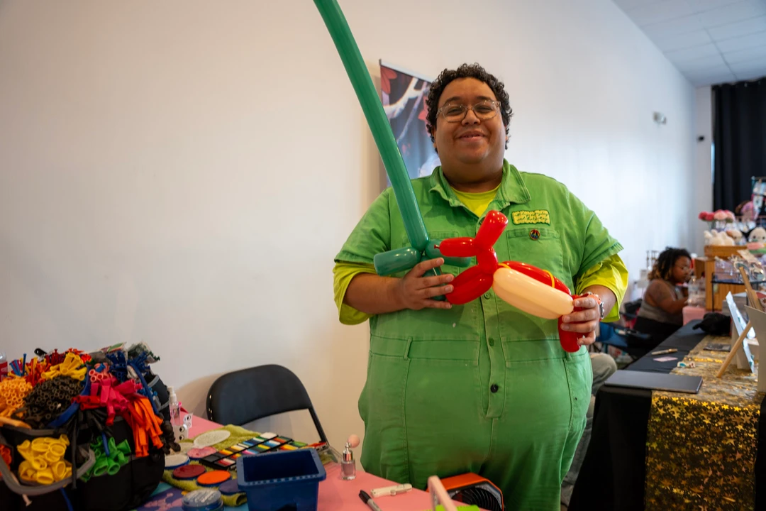 A balloon artist in green holding a balloon creation.