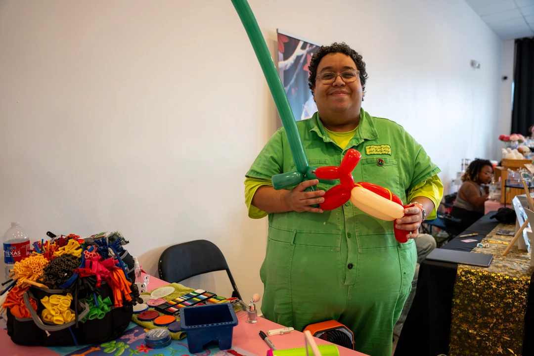 A balloon artist in green holding a balloon creation.