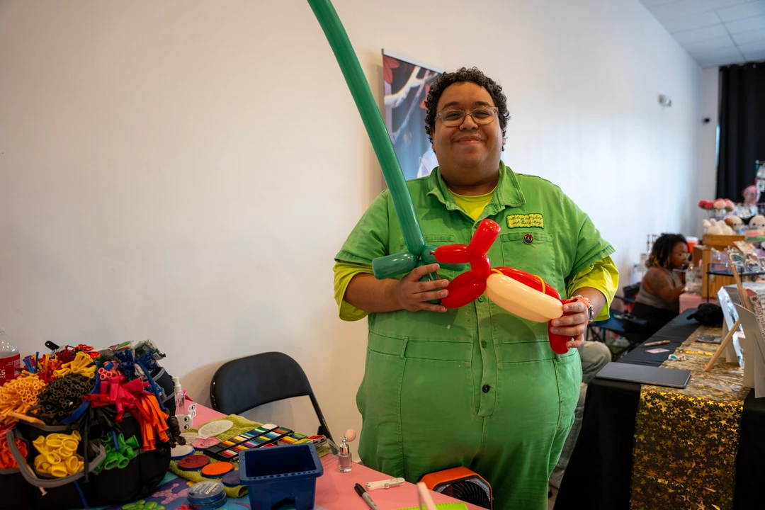 A balloon artist in green holding a balloon creation.