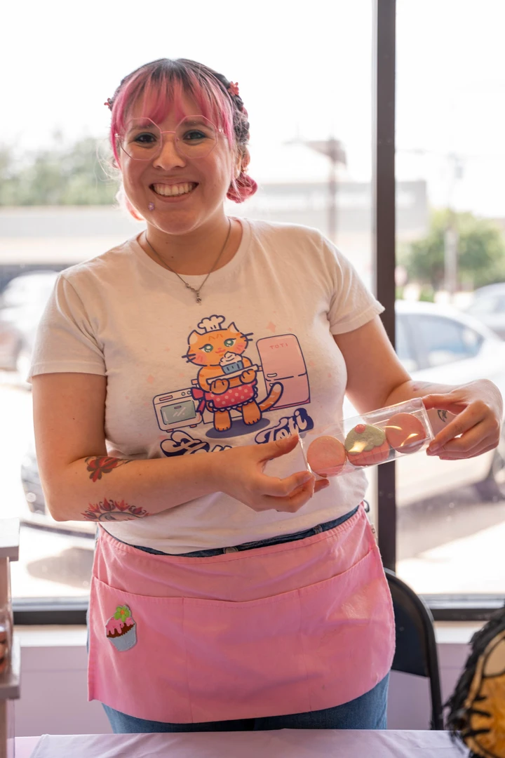 A maker in a pink apron holding a decorated treat.