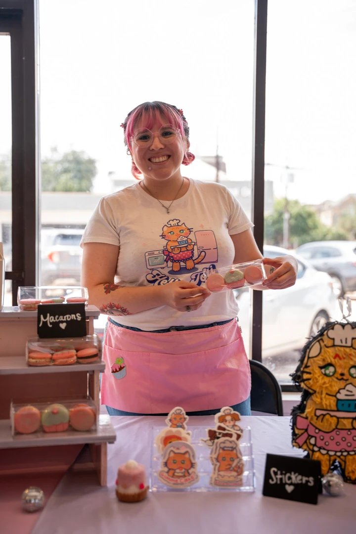 A maker in a pink apron holding a decorated treat.