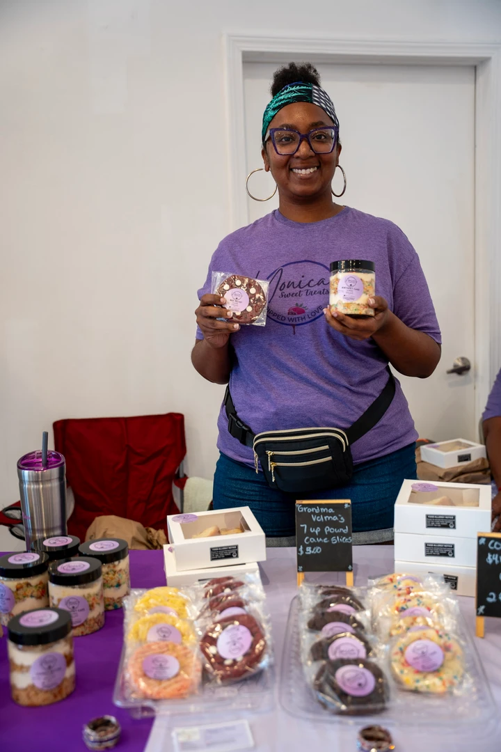 A baker holding dessert jars behind a purple display.