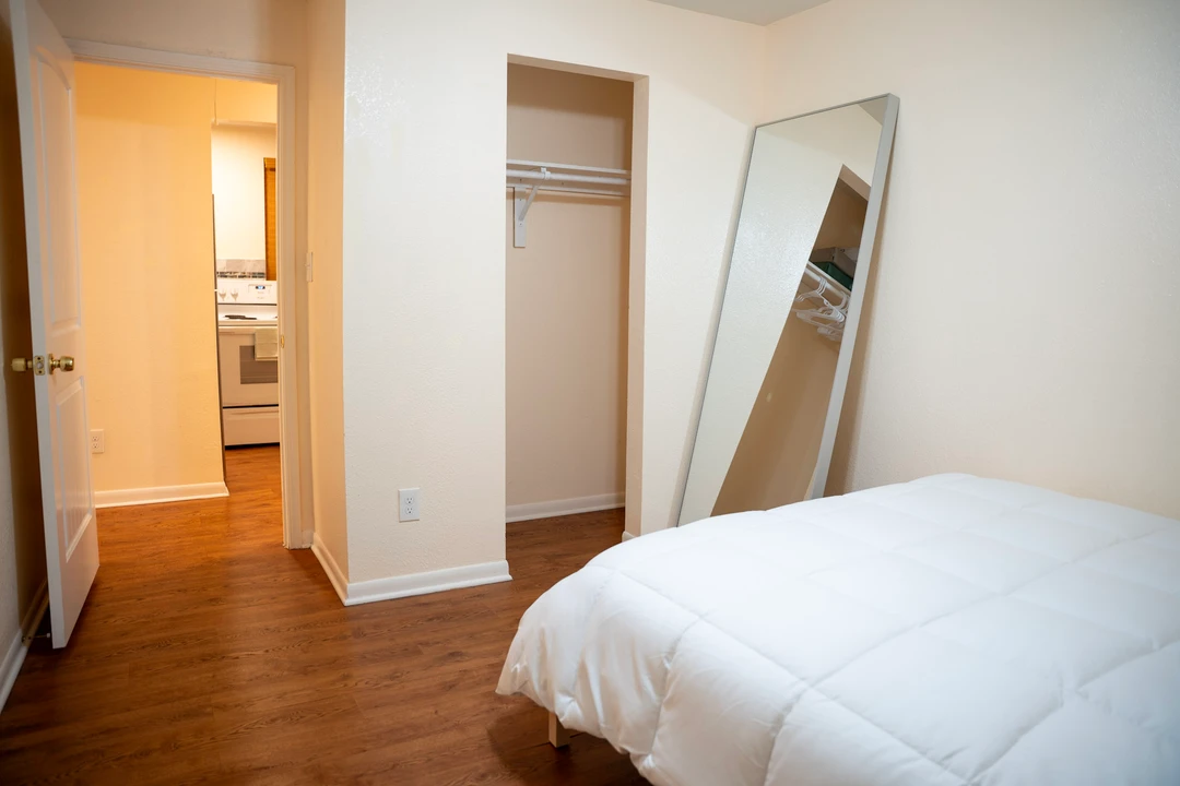 A bedroom with a white bed, tall mirror, and open closet.