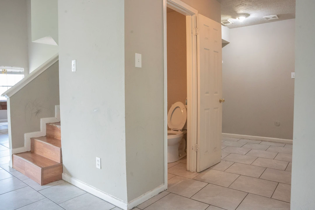 A tiled hallway connects a staircase and a downstairs bathroom.