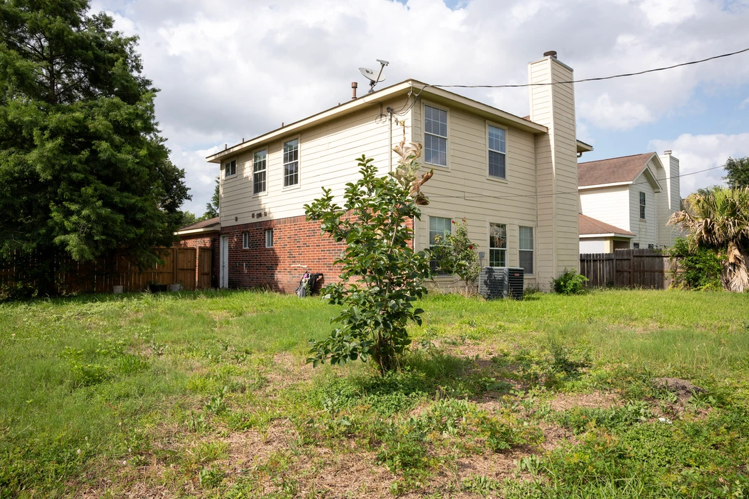 A two-story house and fenced backyard under a partly cloudy sky.