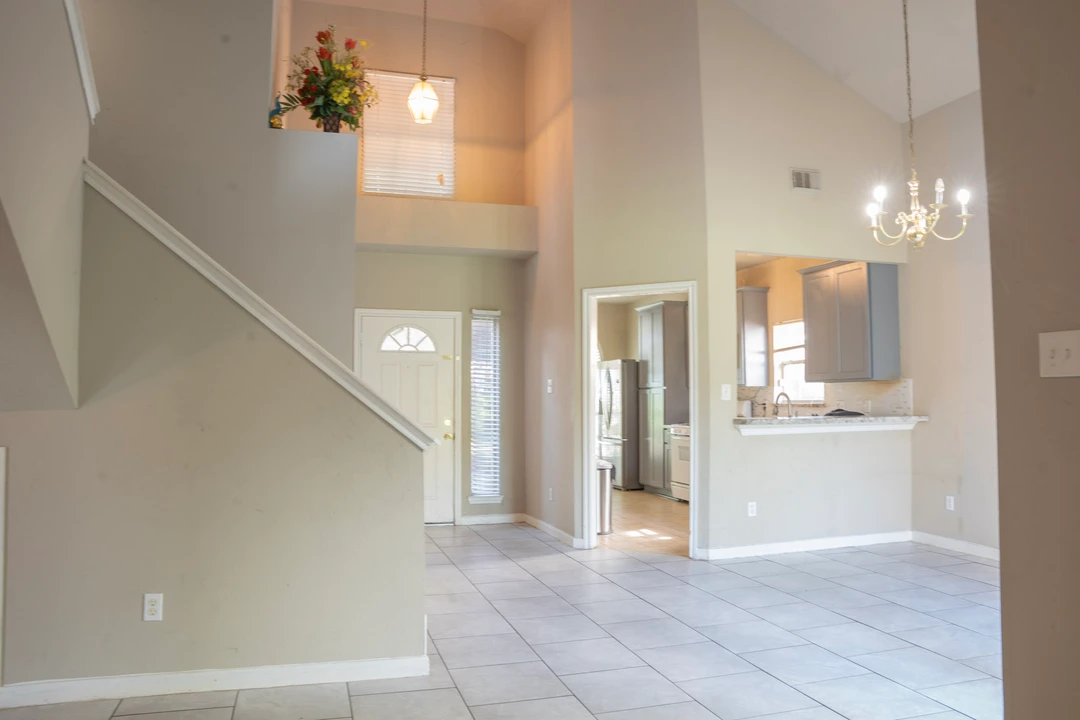 A tall, bright entry and living area with stairs and a view toward the kitchen.