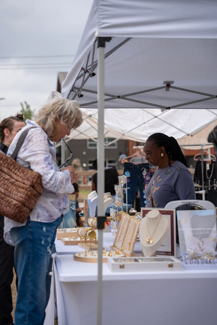 Shoppers browsing a maker’s table beneath a white canopy.