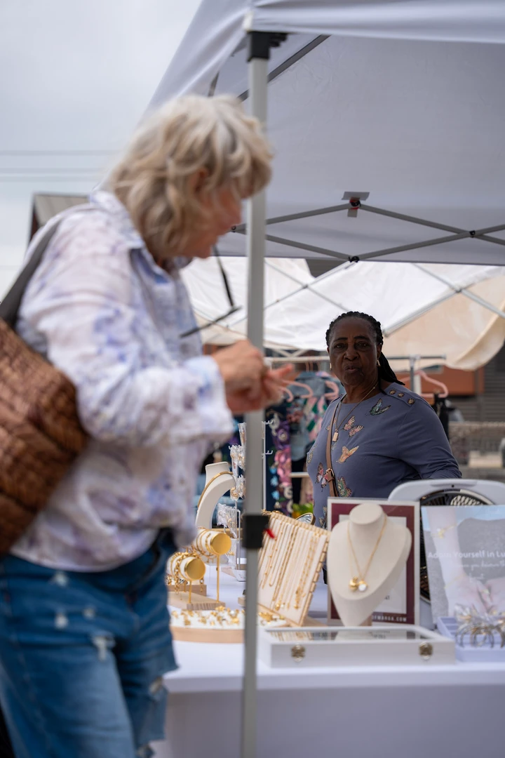 Shoppers browsing a maker’s table beneath a white canopy.