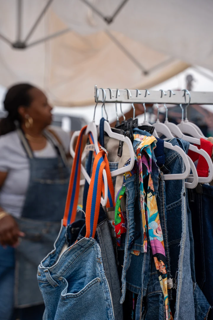 A smiling maker in overalls beside a rack of clothing.