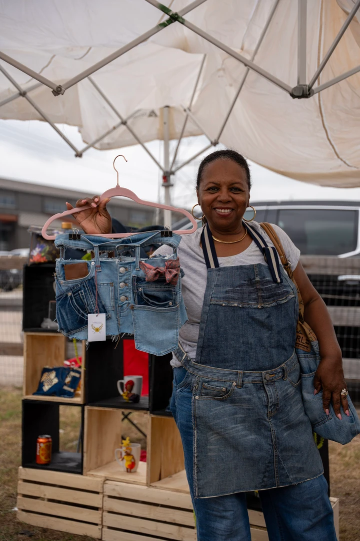 A smiling maker in overalls beside a rack of clothing.
