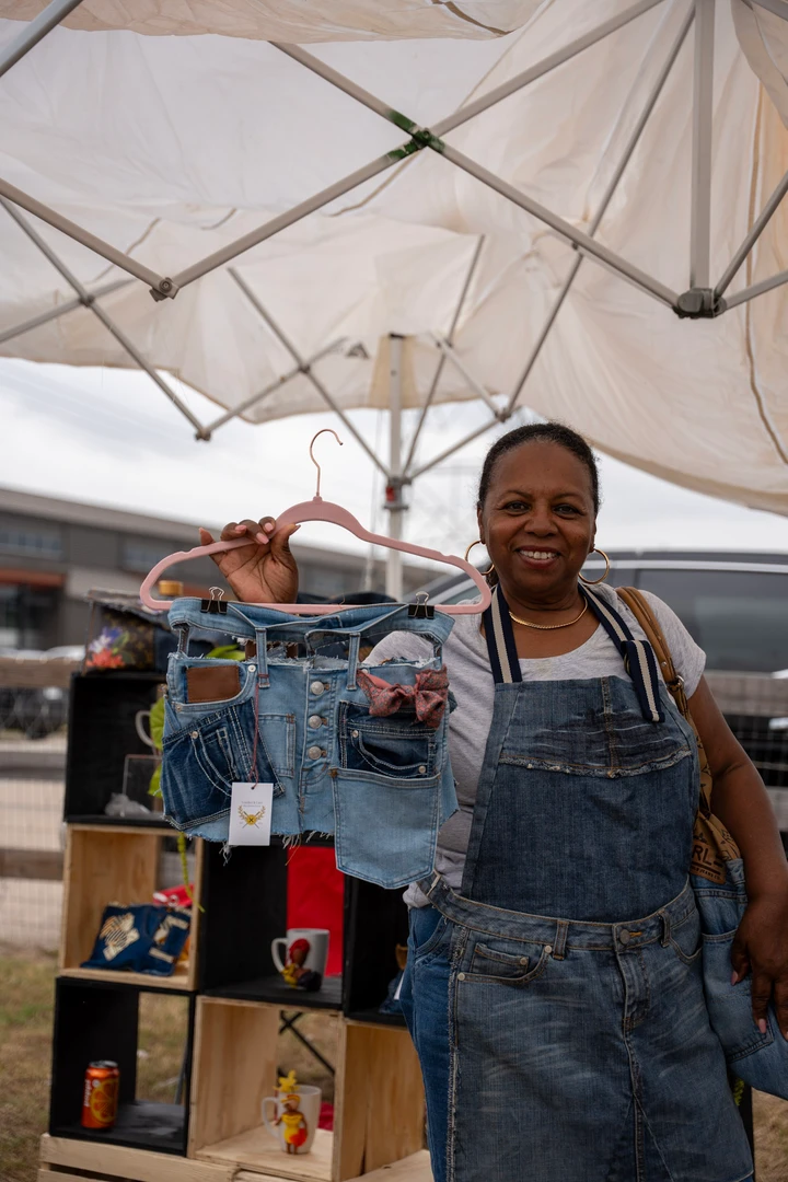 A smiling maker in overalls beside a rack of clothing.