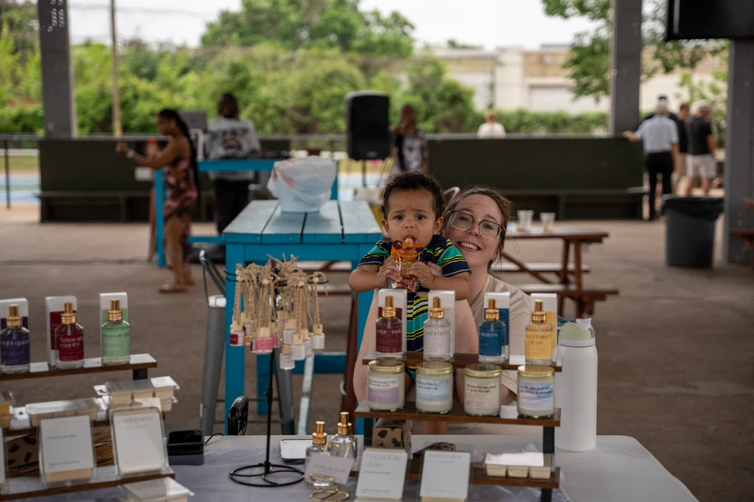 Two makers behind candles and potted plants at an outdoor stall.