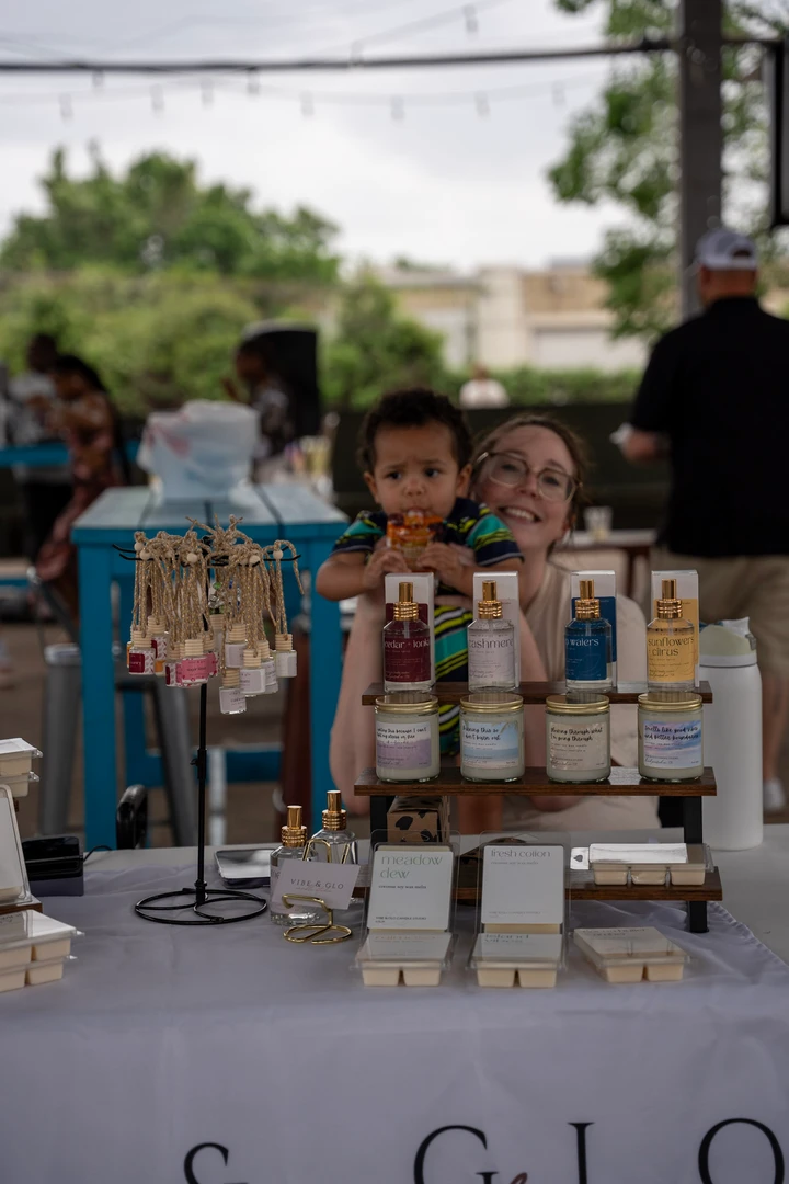 Two makers behind candles and potted plants at an outdoor stall.