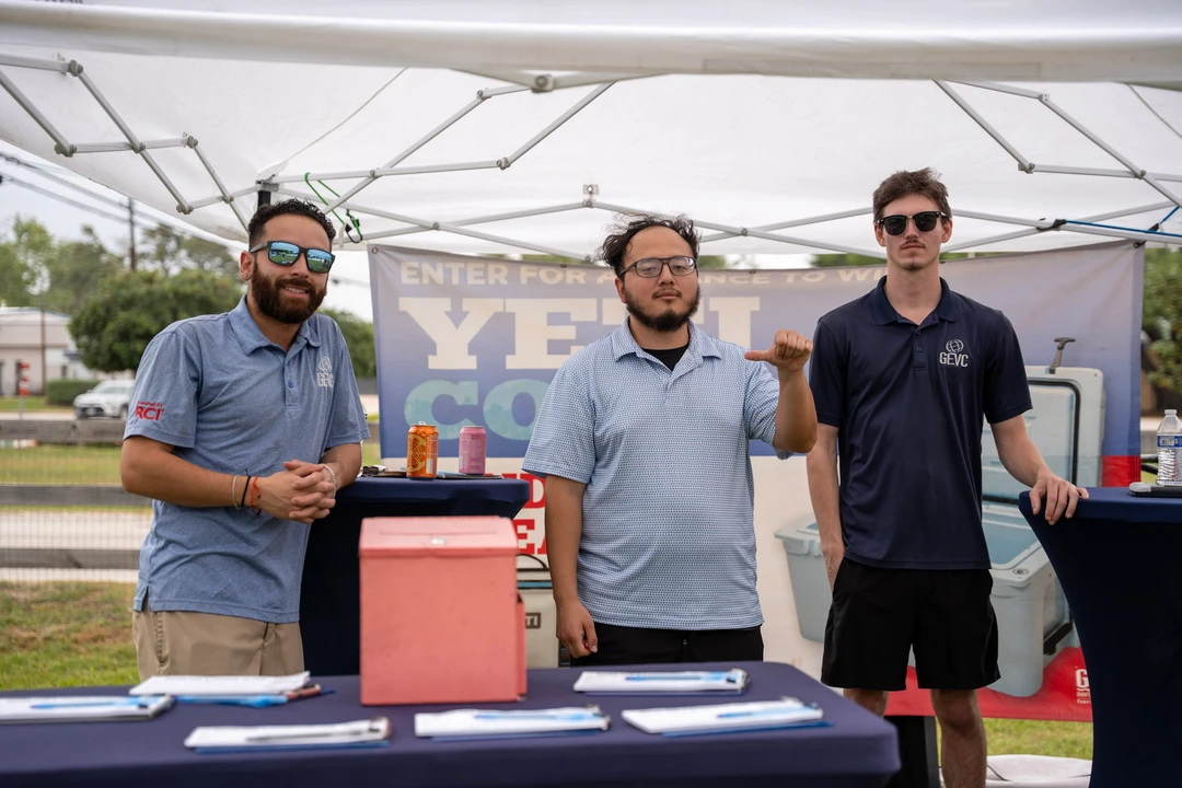 Three vendors standing behind their outdoor beverage table.