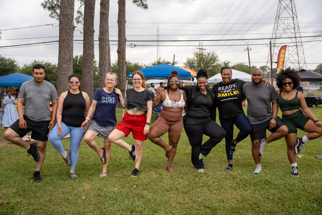 Market visitors balancing in tree pose together on the lawn.