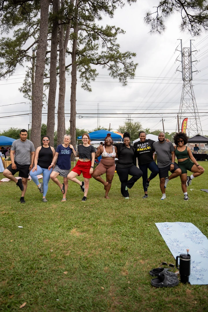 Market visitors balancing in tree pose together on the lawn.
