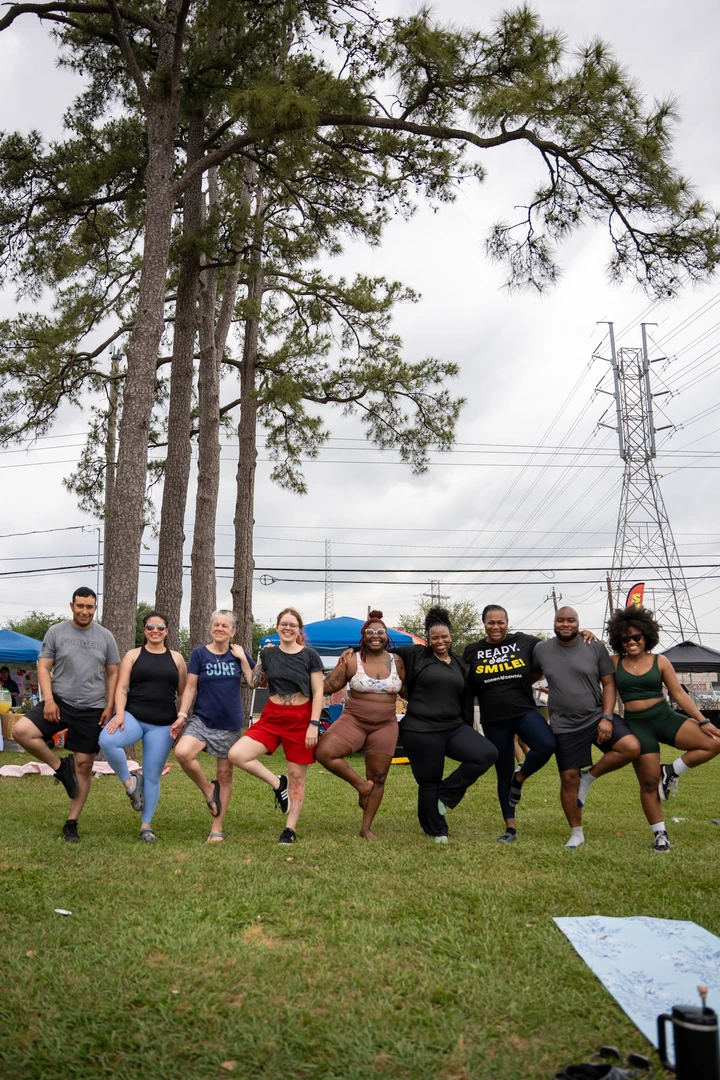 Market visitors balancing in tree pose together on the lawn.
