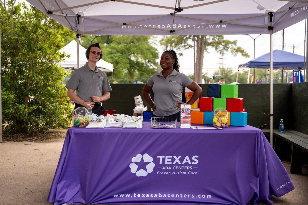 Vendors behind a purple Texas-branded table at the outdoor market.