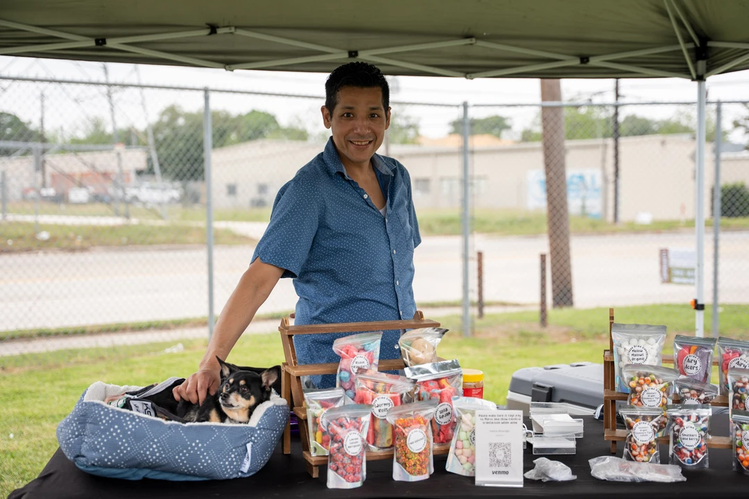A smiling vendor in blue behind a table of packaged sweets.