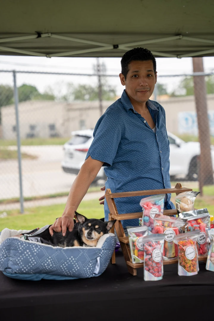 A smiling vendor in blue behind a table of packaged sweets.