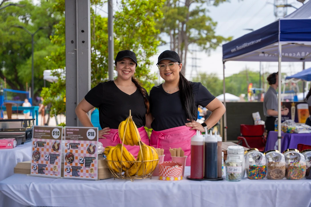 Two makers behind a table of colorful jars and drinks.