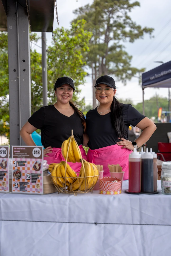 Two makers behind a table of colorful jars and drinks.