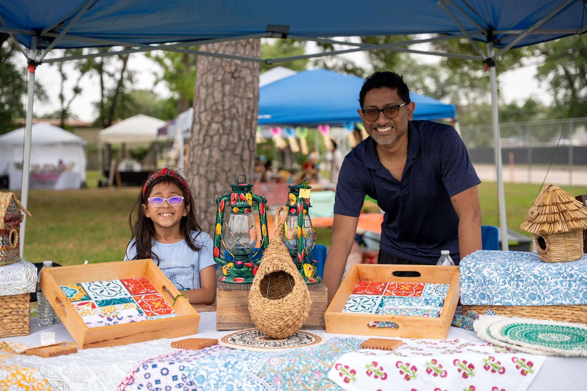 Two makers smile behind a table of handmade birdhouses and colorful goods.