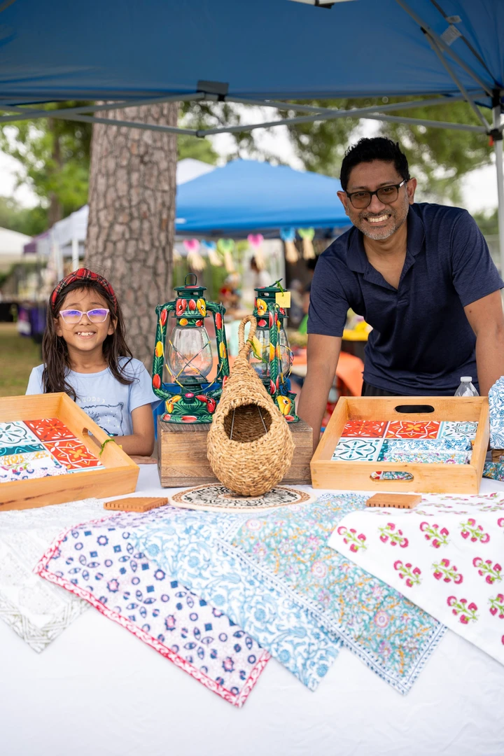 Two makers behind a table of handmade birdhouses and colorful goods.