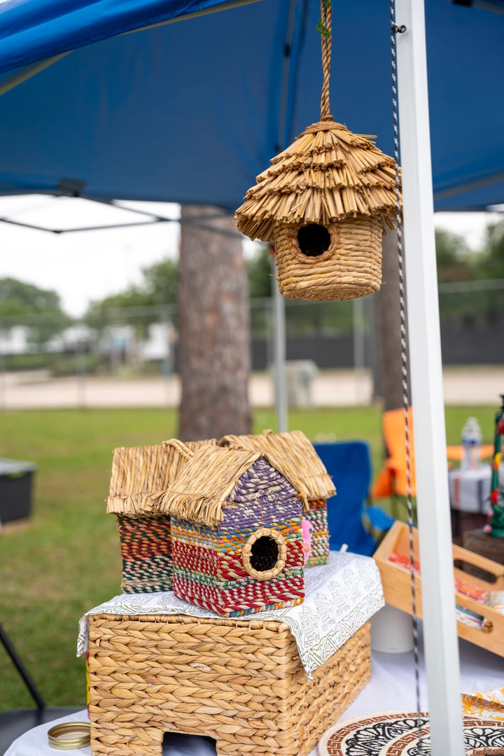 Woven and wooden birdhouses displayed beneath a market canopy.
