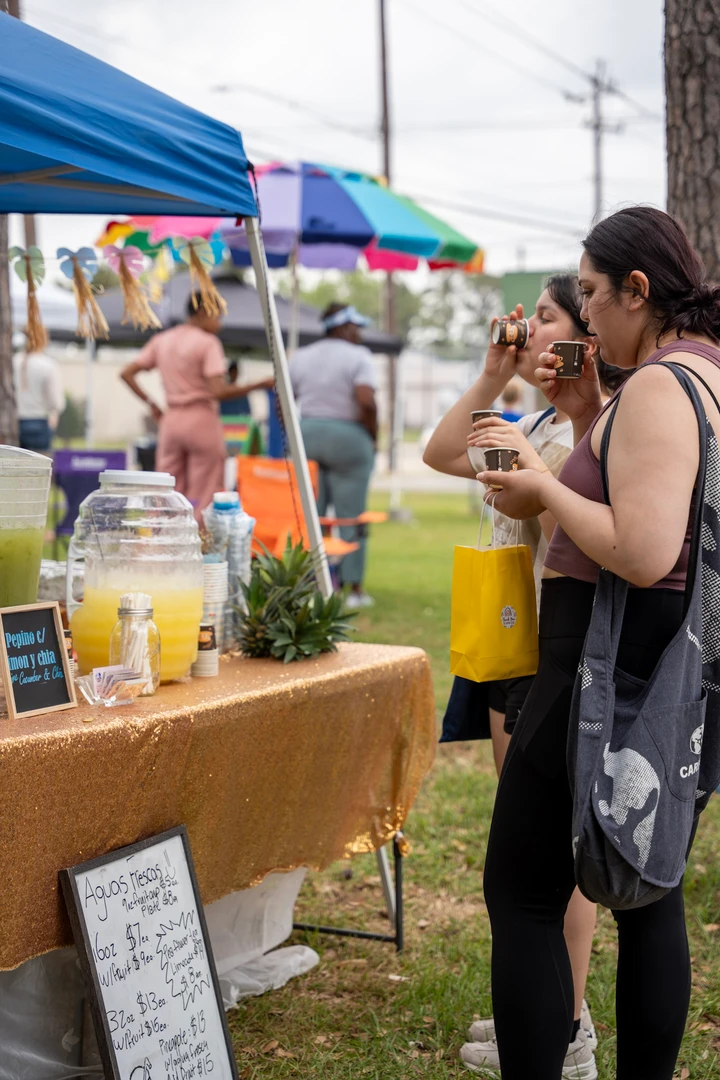 Visitors chat with a drink vendor beneath a rainbow umbrella.