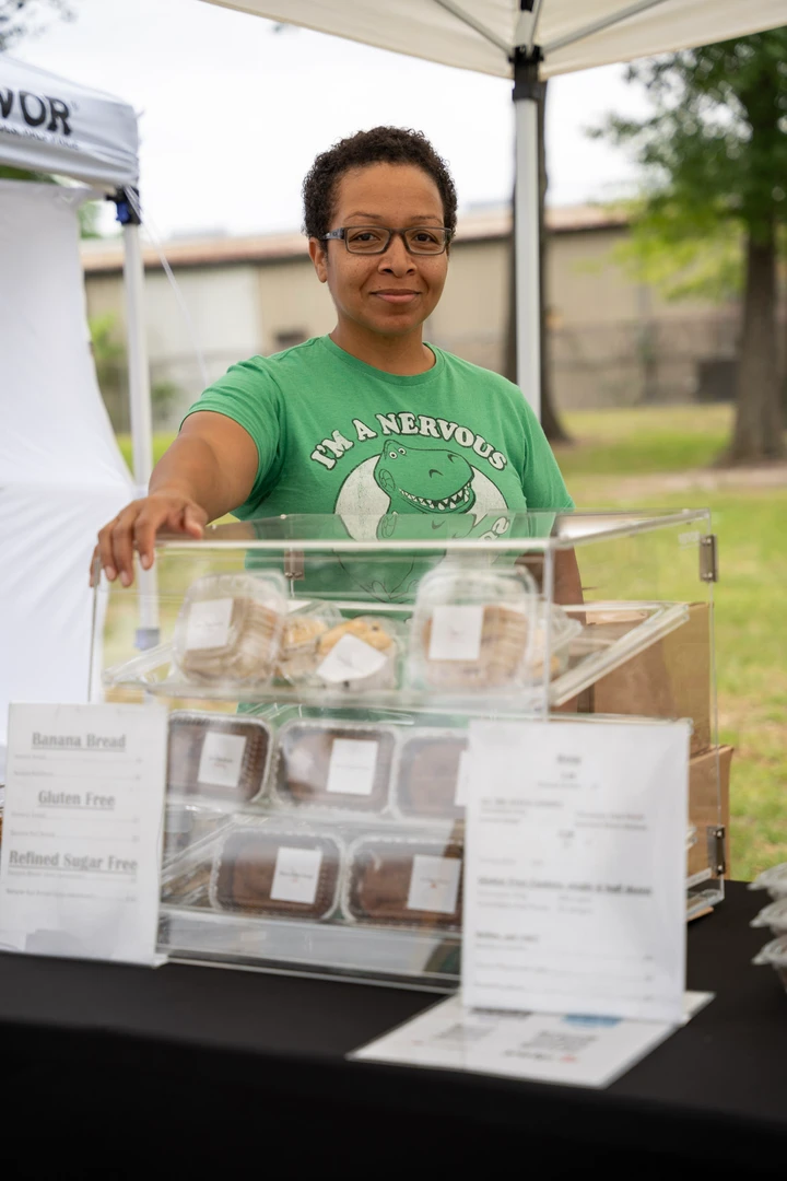 A smiling baker in green behind a clear display of baked goods.