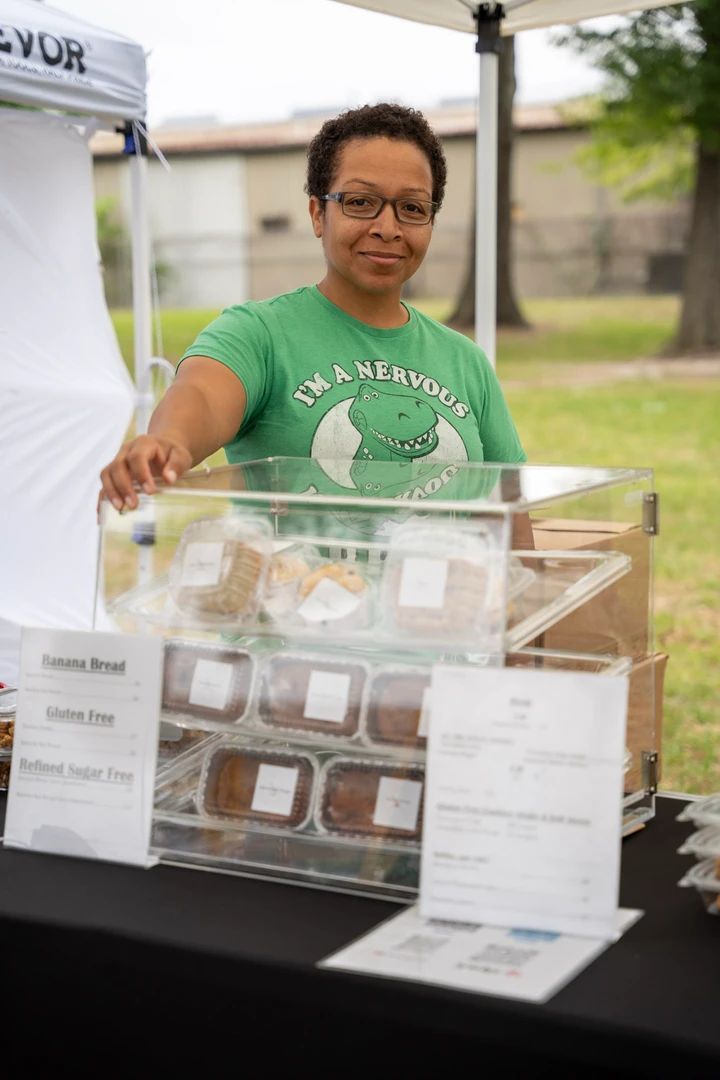 A smiling baker in green behind a clear display of baked goods.