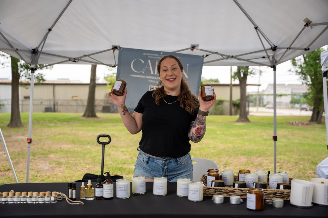 A smiling maker in black behind a table of small glass jars.