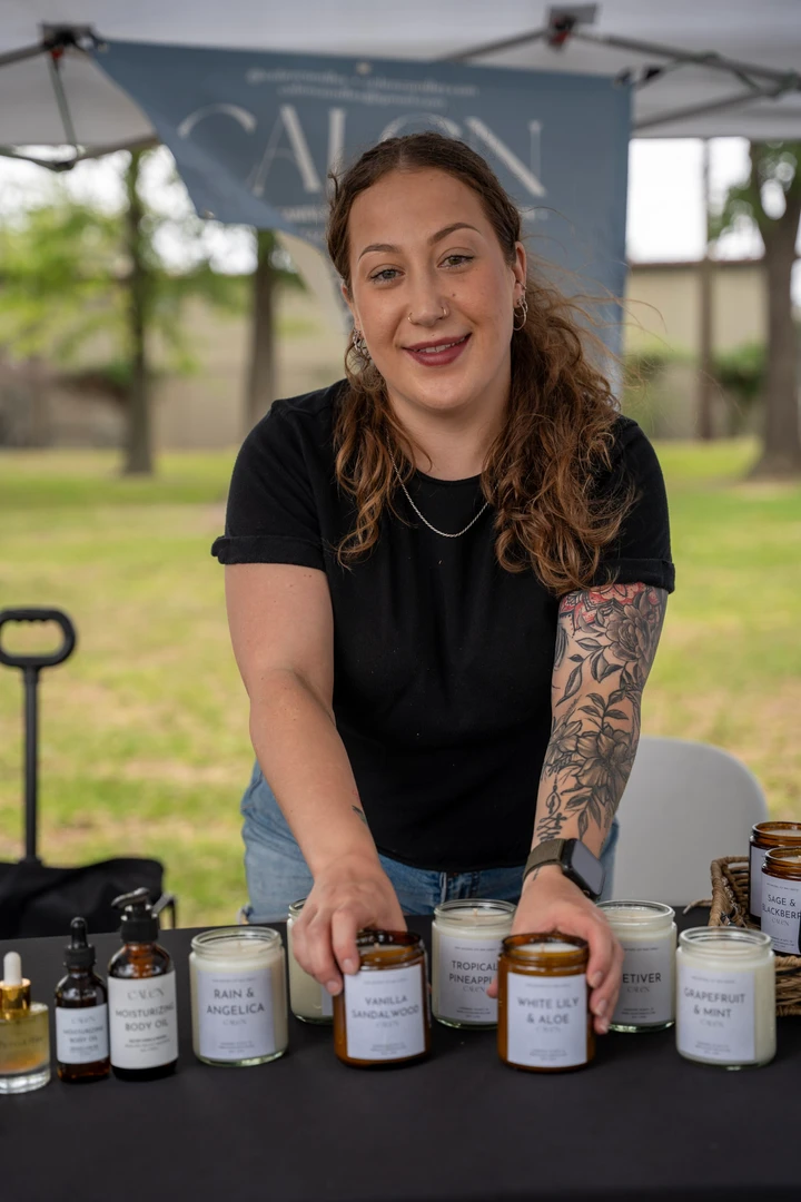A smiling maker leans over a table of small glass jars.