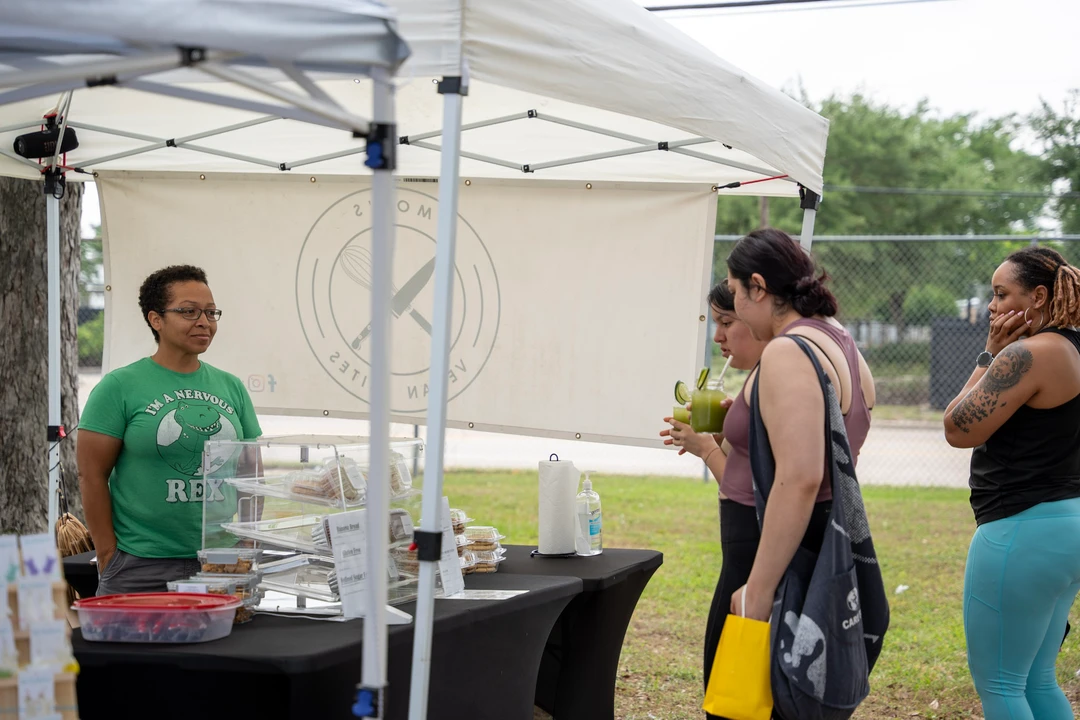 Visitors chatting with a baker beneath a white canopy.