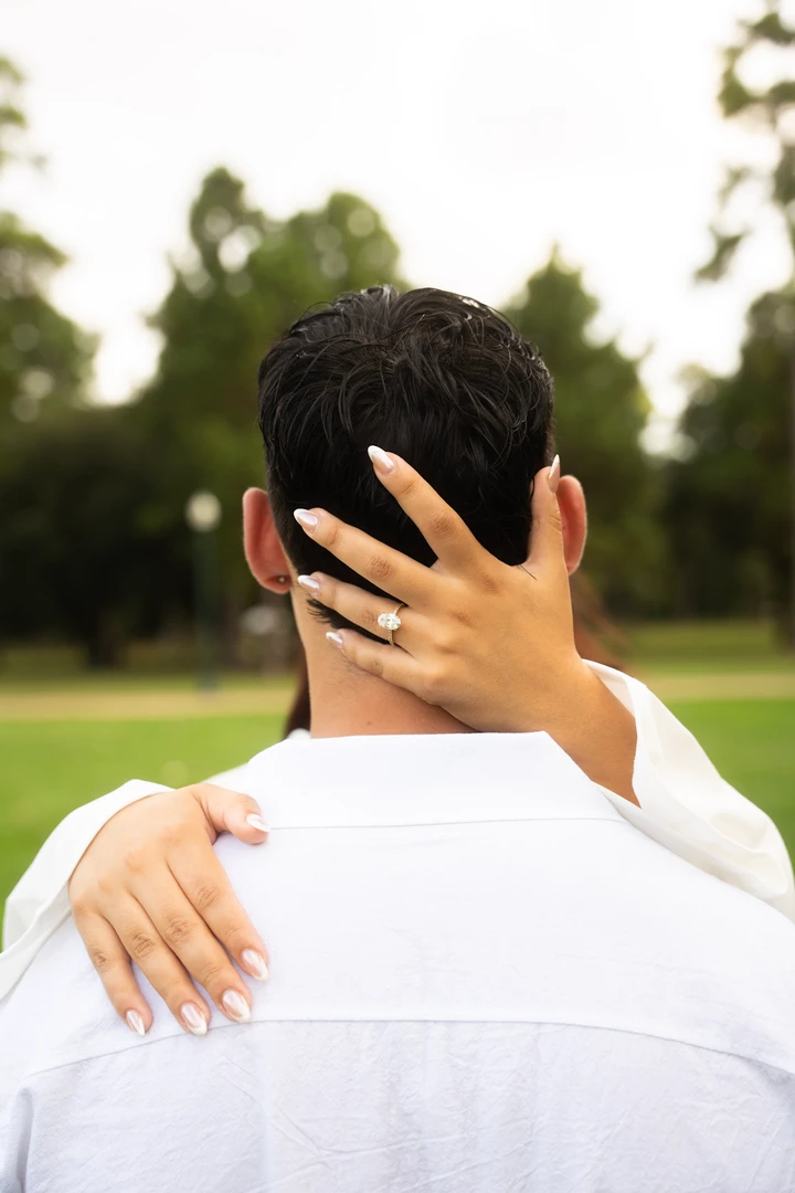 An engagement ring rests against a partner’s shoulder during an embrace.