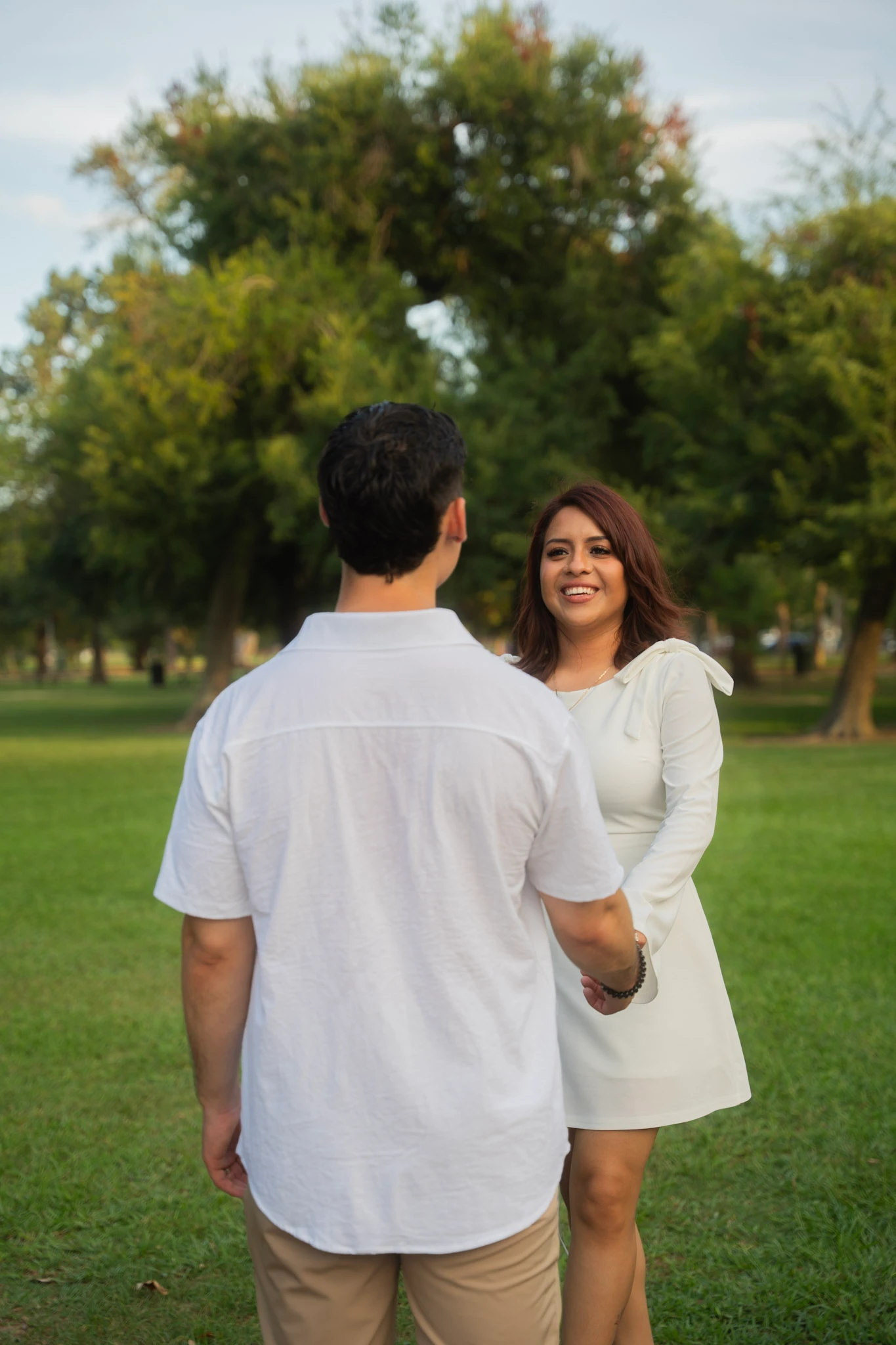 A couple face each other and hold hands in a green park.
